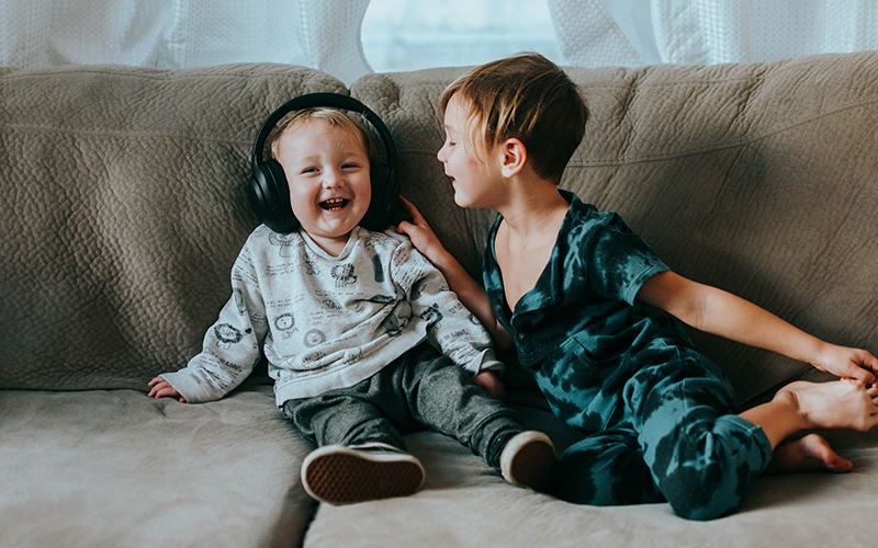 Two children sitting on the couch listening to music 